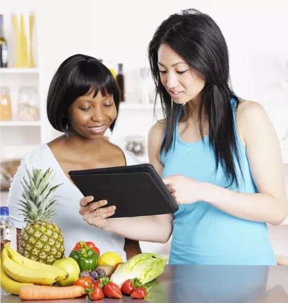 A nutritionist and registered dietician checking food choices on a tab, with a table surrounded with fruits and vegetables